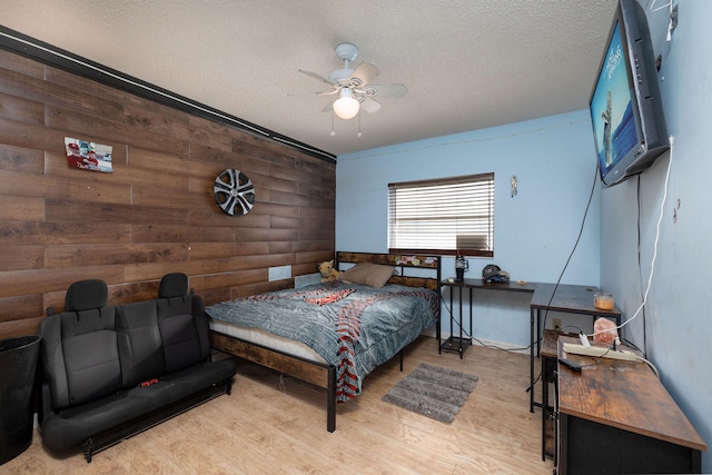 bedroom with ceiling fan, a textured ceiling, wooden walls, and light hardwood / wood-style floors