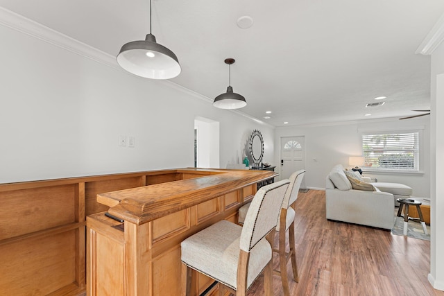 dining space featuring bar, light hardwood / wood-style flooring, and crown molding