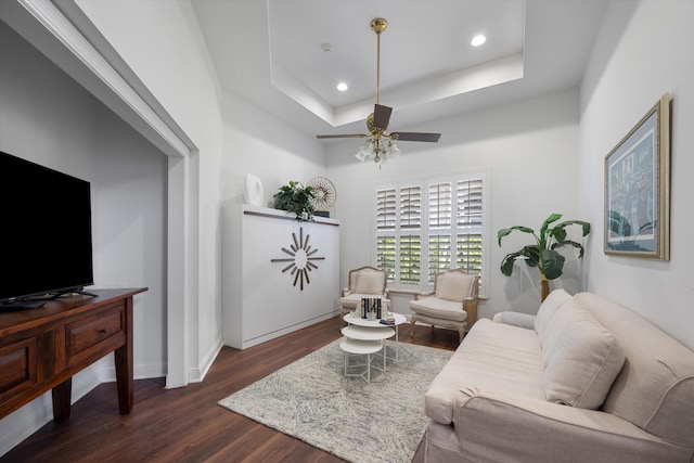 living room with dark hardwood / wood-style floors, a tray ceiling, and ceiling fan