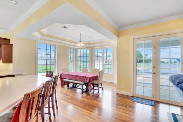 dining room featuring light hardwood / wood-style floors, crown molding, a tray ceiling, french doors, and a notable chandelier