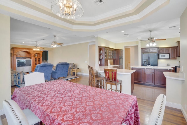 dining room featuring ceiling fan with notable chandelier, light wood-type flooring, a raised ceiling, and crown molding