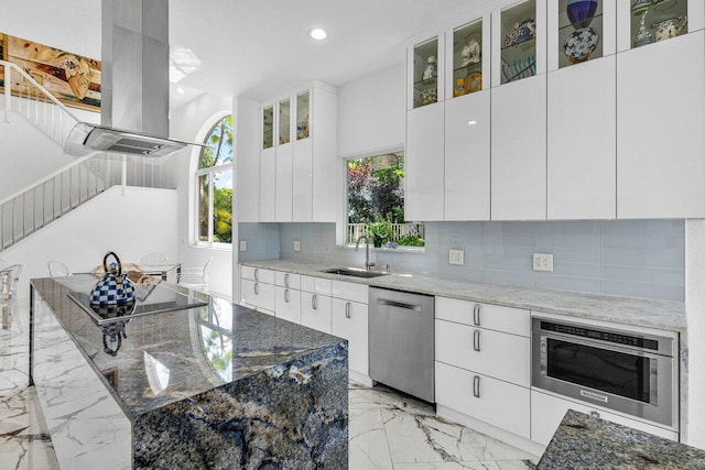 kitchen featuring stainless steel appliances, dark stone counters, white cabinets, sink, and island exhaust hood