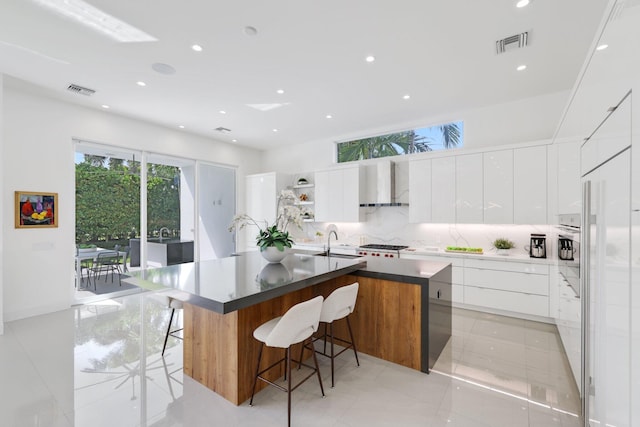 kitchen featuring a kitchen island with sink, backsplash, white cabinets, a kitchen bar, and light tile patterned floors