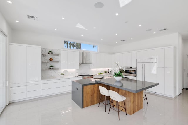 kitchen with wall chimney range hood, white cabinetry, a kitchen breakfast bar, and a spacious island