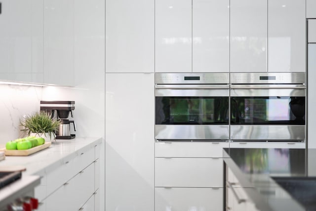 kitchen featuring stainless steel oven, light stone counters, and white cabinetry