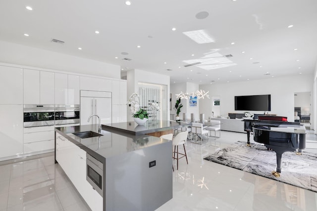 kitchen with a large island with sink, white cabinets, sink, built in appliances, and a kitchen breakfast bar