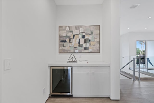 bar featuring light wood-type flooring, wine cooler, and white cabinets