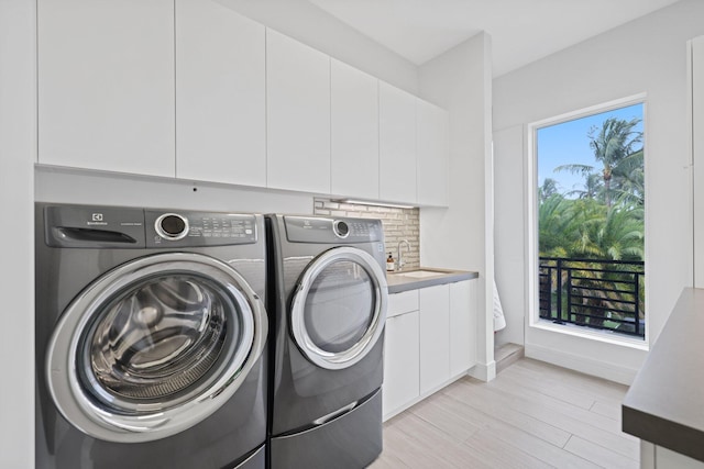 laundry area featuring cabinets, light wood-type flooring, sink, and washing machine and clothes dryer