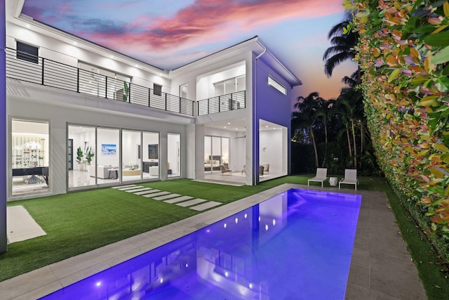 pool at dusk with a patio and a yard