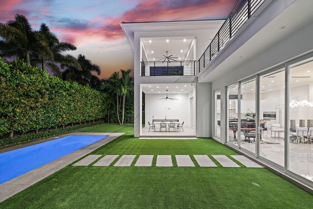 pool at dusk featuring ceiling fan, a lawn, and a patio