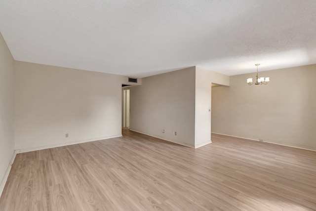 spare room featuring light wood-type flooring, a chandelier, and baseboards