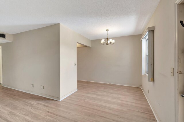 spare room with light wood-style floors, a chandelier, a textured ceiling, and baseboards