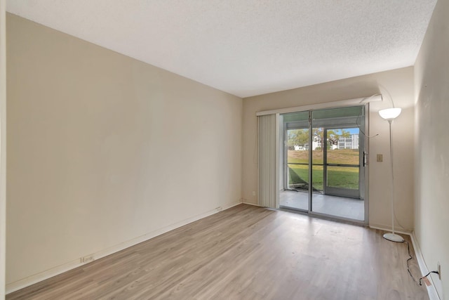 empty room featuring light wood finished floors, baseboards, and a textured ceiling