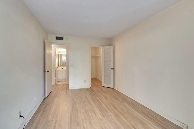 unfurnished bedroom featuring light wood finished floors, a walk in closet, baseboards, and a closet
