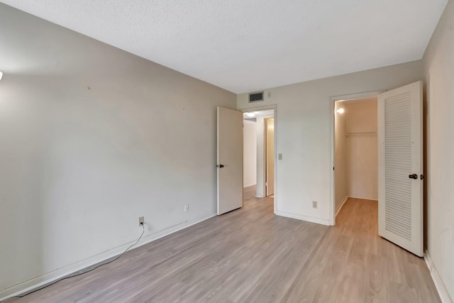 unfurnished bedroom featuring light wood-type flooring, a spacious closet, a closet, and baseboards
