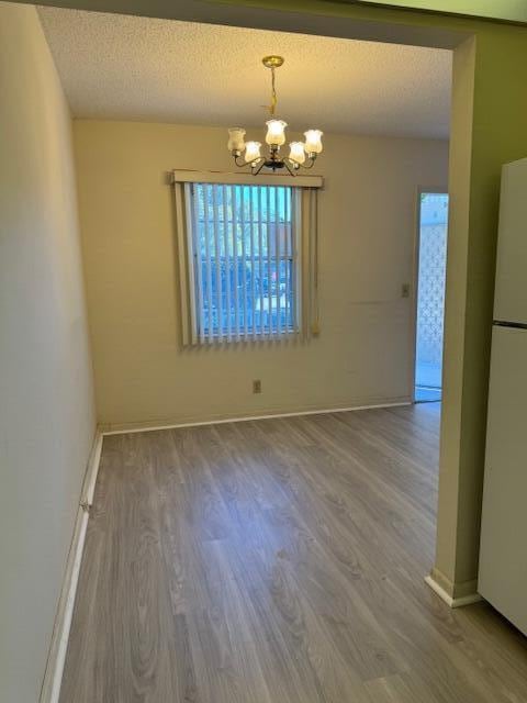 unfurnished dining area with a textured ceiling, hardwood / wood-style flooring, and an inviting chandelier