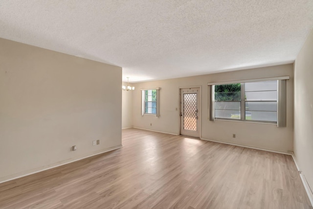 unfurnished living room featuring a chandelier, light wood-type flooring, a textured ceiling, and baseboards
