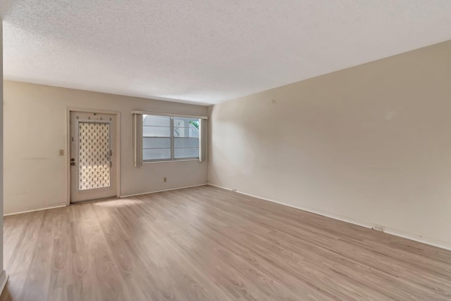spare room with light wood-type flooring, a textured ceiling, and baseboards