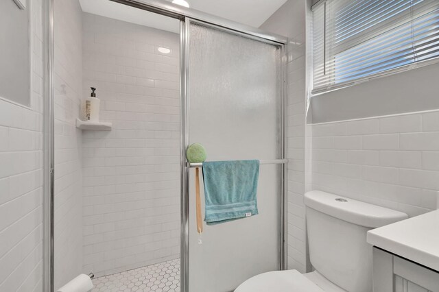 bathroom with vanity, toilet, tile walls, and walk in shower