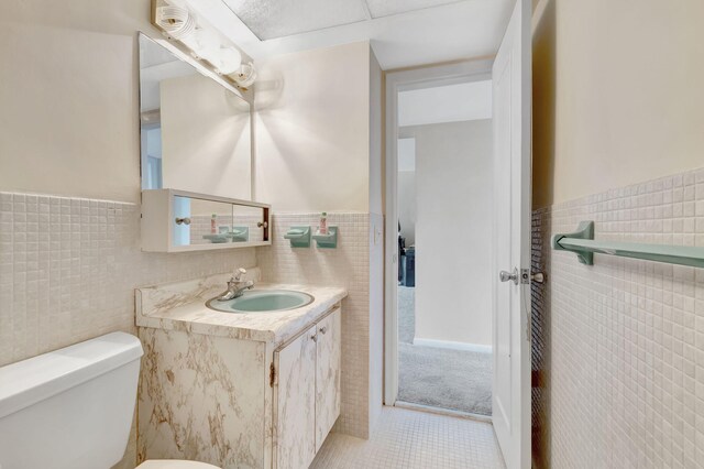 bathroom with tile walls, toilet, vanity, and tile patterned flooring