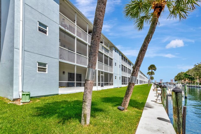 dock area with a water view, a lawn, and a balcony