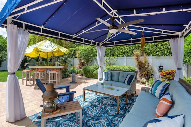 view of patio featuring a ceiling fan, an outdoor living space, a fenced backyard, a gazebo, and outdoor dry bar