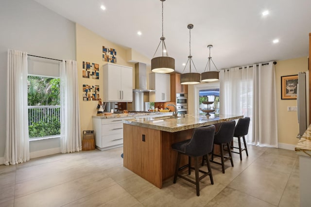 kitchen with a large island, decorative light fixtures, a kitchen breakfast bar, white cabinetry, and wall chimney exhaust hood