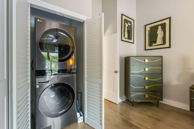 laundry area featuring laundry area, stacked washer / dryer, wood finished floors, and baseboards