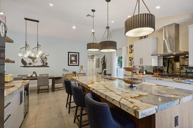 kitchen with visible vents, a large island with sink, stainless steel gas stovetop, pendant lighting, and wall chimney exhaust hood