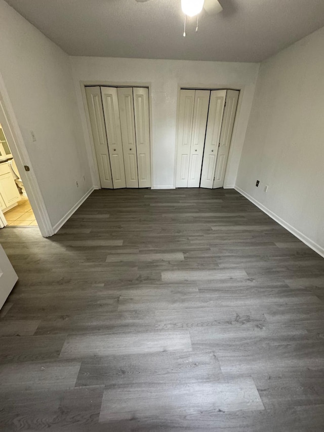 unfurnished bedroom featuring dark hardwood / wood-style floors, ceiling fan, and multiple closets