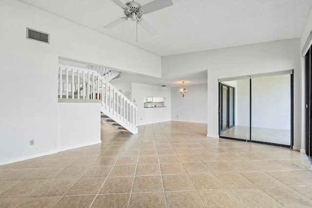 unfurnished living room with ceiling fan with notable chandelier, light tile patterned floors, a textured ceiling, and a high ceiling