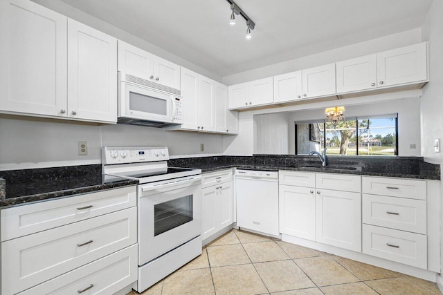 kitchen with white appliances, dark stone counters, sink, light tile patterned floors, and white cabinetry