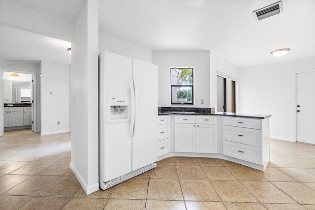 kitchen with white refrigerator with ice dispenser, white cabinets, dark stone countertops, light tile patterned floors, and kitchen peninsula