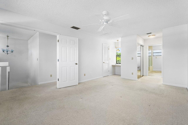 carpeted empty room featuring ceiling fan with notable chandelier and a textured ceiling