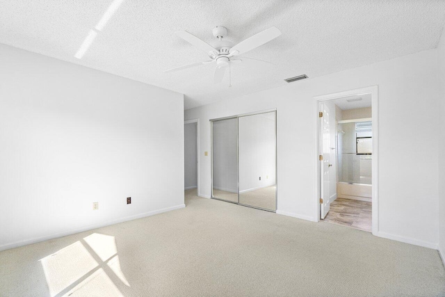 unfurnished bedroom featuring light carpet, ensuite bath, a textured ceiling, ceiling fan, and a closet