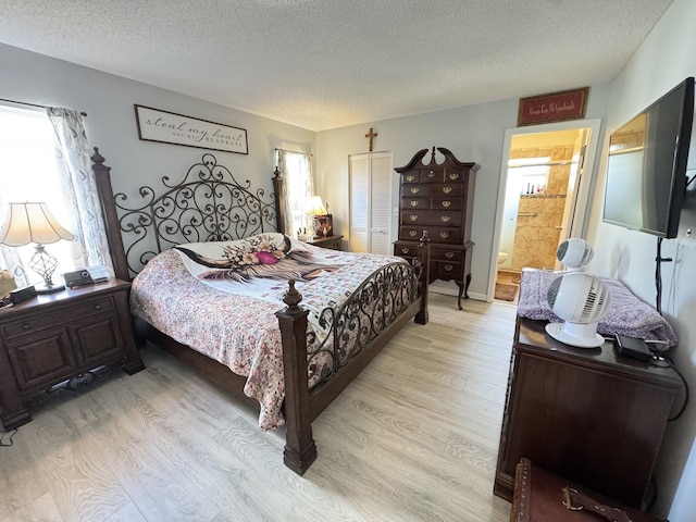 bedroom with multiple windows, ensuite bath, a textured ceiling, and light hardwood / wood-style flooring