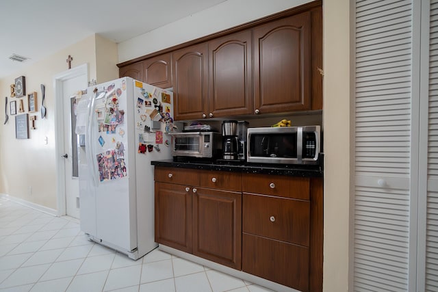 kitchen with dark stone countertops, light tile patterned floors, and white refrigerator with ice dispenser