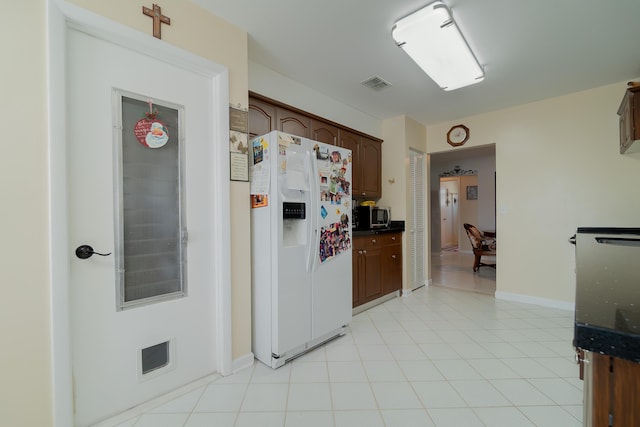 kitchen with dark brown cabinets, white fridge with ice dispenser, and light tile patterned floors