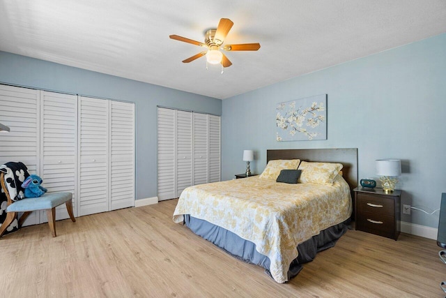 bedroom with ceiling fan, multiple closets, and light hardwood / wood-style flooring