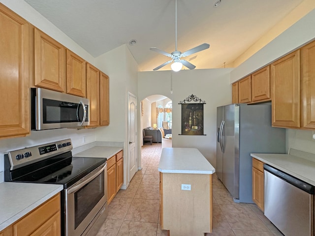 kitchen with ceiling fan, light tile patterned flooring, a kitchen island, stainless steel appliances, and vaulted ceiling