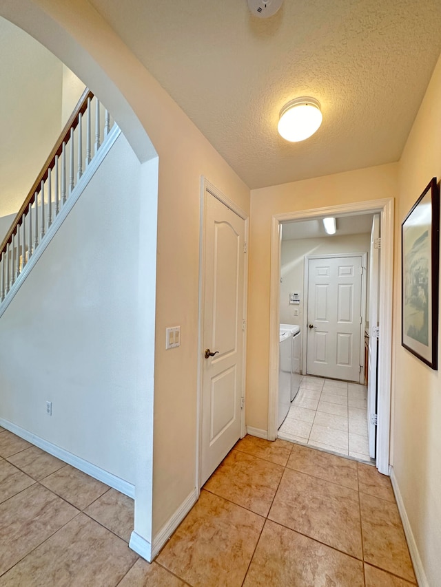 corridor featuring a textured ceiling, light tile patterned floors, and washing machine and dryer