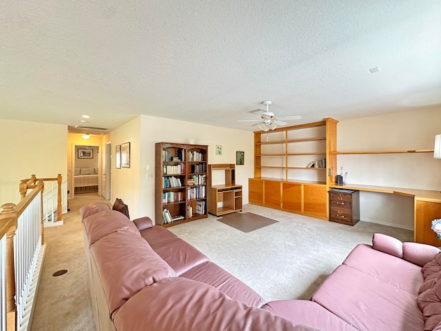 living room featuring ceiling fan, light colored carpet, a textured ceiling, and built in desk