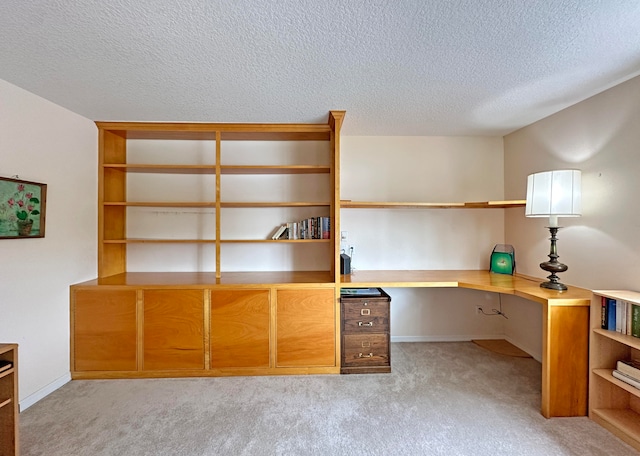 unfurnished office with built in desk, a textured ceiling, and light colored carpet