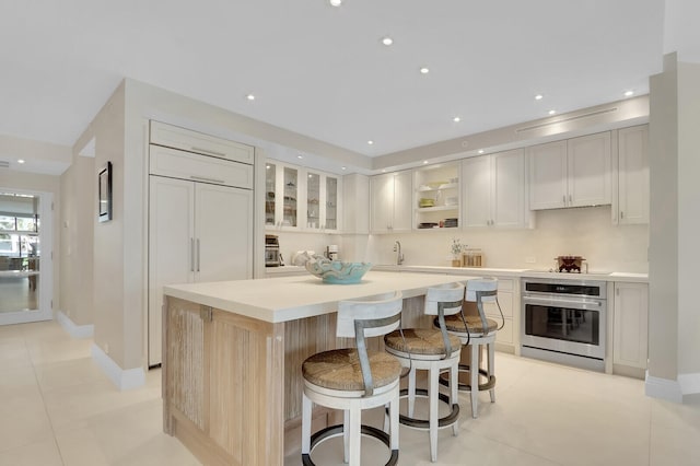 kitchen with white cabinetry, a breakfast bar, stainless steel oven, a center island, and sink