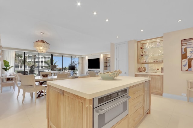 kitchen featuring stainless steel oven, decorative light fixtures, light brown cabinetry, and a notable chandelier