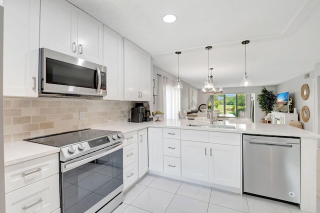 kitchen featuring sink, kitchen peninsula, white cabinetry, appliances with stainless steel finishes, and a notable chandelier