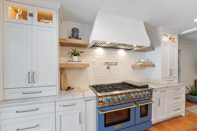 kitchen featuring light stone counters, white cabinets, custom range hood, range with two ovens, and crown molding