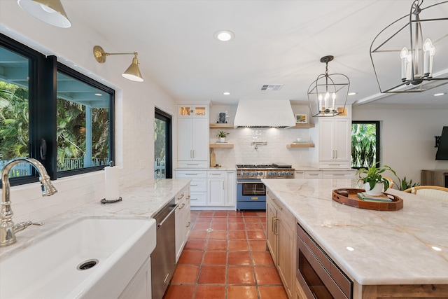 kitchen featuring custom exhaust hood, an inviting chandelier, a sink, open shelves, and appliances with stainless steel finishes