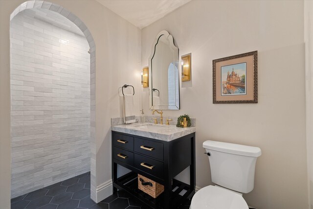 bathroom featuring toilet, tile patterned flooring, vanity, and tiled shower