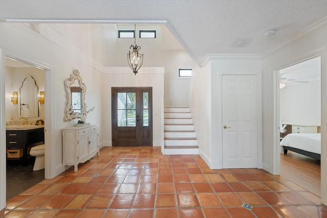 foyer featuring a textured ceiling, light tile patterned flooring, ornamental molding, and stairs